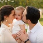 Happy couple kissing their smiling baby outdoors.