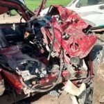 Red car severely damaged in a crash with a crushed front end and debris scattered across the scene.