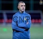 Man in blue sportswear standing with arms crossed on a soccer field.