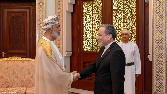 ar - Center News Network Two men shake hands in an ornate room; one in traditional Omani attire and the other in a dark suit, with a uniformed attendant in the background.