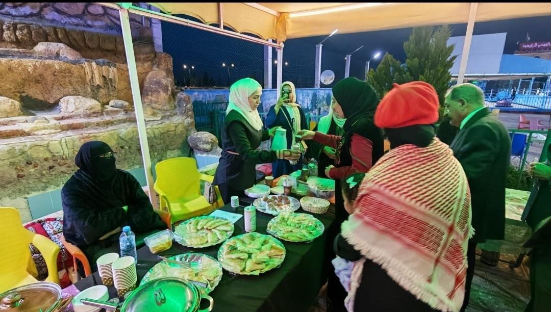 Group of people wearing head coverings around a table of food at an outdoor night event under a yellow canopy.