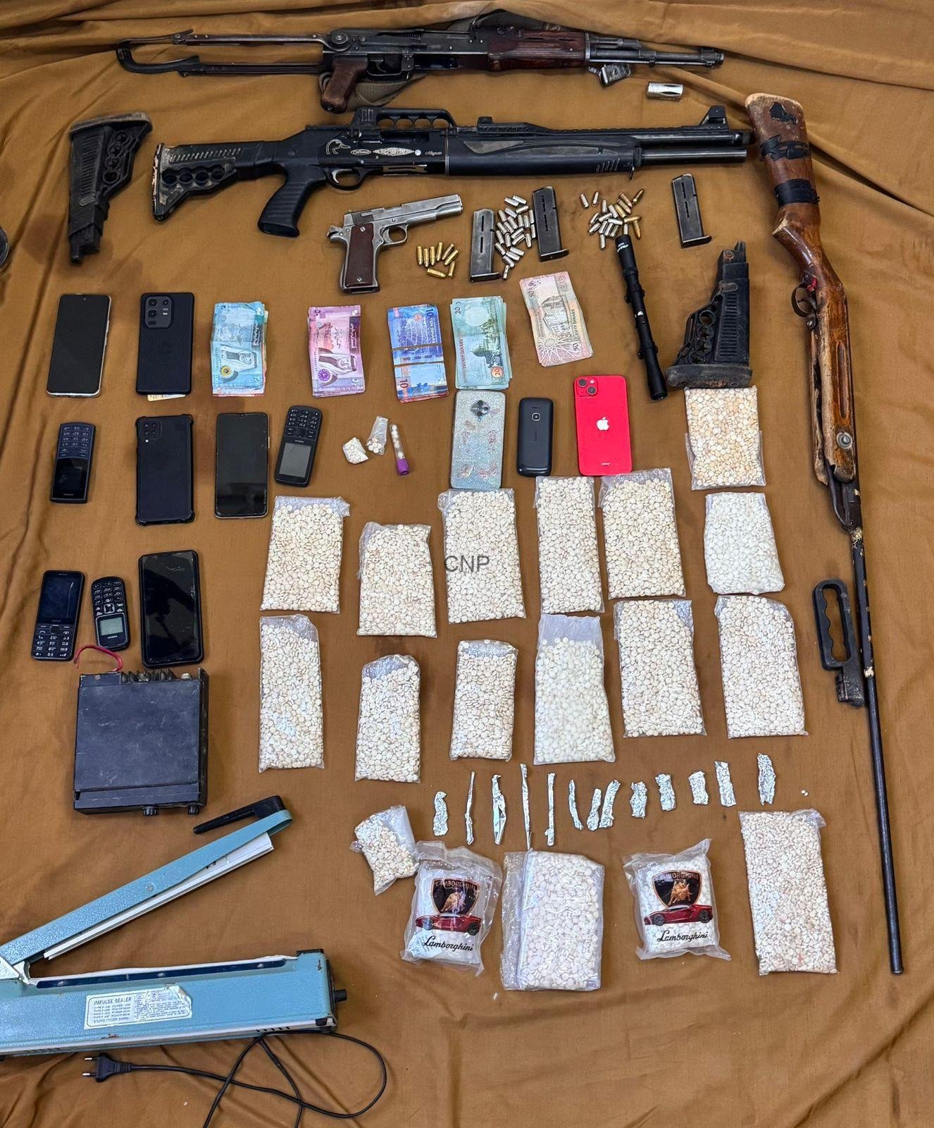 dd - Center News Network Weapon and contraband stash: several firearms, magazines, and ammunition laid out with money and phones on a brown backdrop for display or evidence.