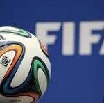 Soccer ball with multicolored panels in front of a blue FIFA backdrop.