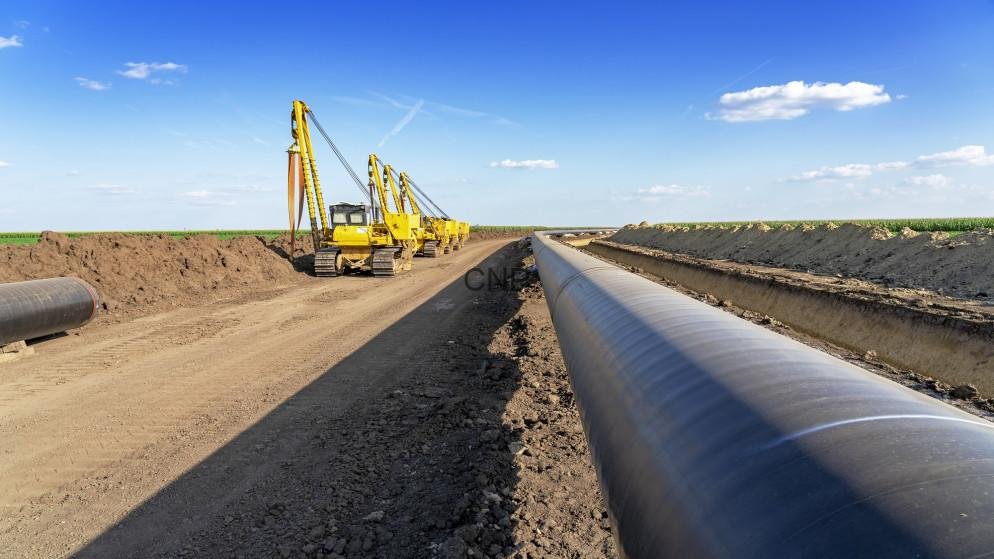gaz - Center News Network Yellow excavators lay a large underground pipeline along a dirt road under a blue sky, during construction.