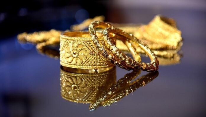 Close-up of ornate gold bracelets and rings on a mirrored surface, with floral engravings and reflections.