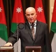 Bald man in a suit delivering a speech at a podium, microphone in front, with red flags and white stars in the background.