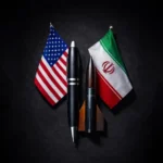 Flag of the United States and Iran displayed beside three pens on a dark surface.
