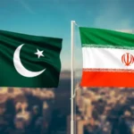 Two national flags on flagpoles flutter over a city skyline: Pakistan (green with crescent and star) and Iran (green, white, red).