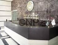 Reception desk in a modern lobby with a dark counter, marble floor, and a circular emblem on the wall behind it; the letters 'CNP' are visible on the glass panel.