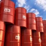 Stacked red oil barrels outdoors under a blue sky with clouds, labeled OIL.