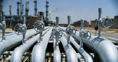 oil - Center News Network Rows of large metal pipelines with circular valve wheels at an oil refinery or processing plant.