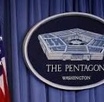 Seal of the Pentagon on a blue curtain backdrop with the U.S. flag to the left.