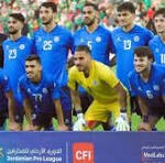 Soccer team in blue jerseys posing for a pre-match group photo on the field; goalkeeper wearing yellow stands in the center.