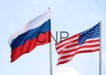rr uu - Center News Network Russia and United States flags waving on flagpoles against a pale blue sky.