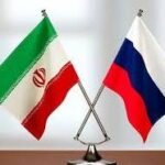 Crossed Iranian and Russian flags on a desk stand, symbolizing diplomatic relations.
