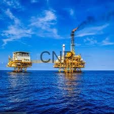 Offshore oil rig platforms standing in the deep blue ocean under a bright sky with a crane visible on one platform.