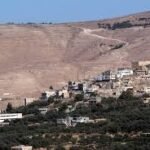 Hilly landscape with a small town of white and beige buildings at the hill’s base, set against a dry, brown hillside.