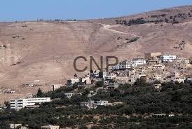 taf - Center News Network Hilly landscape with a small town of white and beige buildings at the hill’s base, set against a dry, brown hillside.