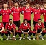 Soccer team in red jerseys posing for a group photo on the field with a stadium full of fans behind them.