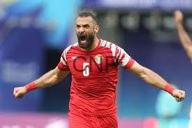 Male footballer in a red kit celebrating with arms outstretched on the pitch.