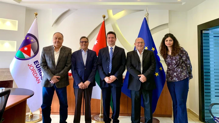 - Center News Network Five businesspeople in suits stand in a diplomatic office with Jordan, Turkey, and EU flags behind them.