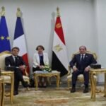 Officials seated in a formal meeting room with European Union, French, and Egyptian flags behind them and ornate gold furniture.