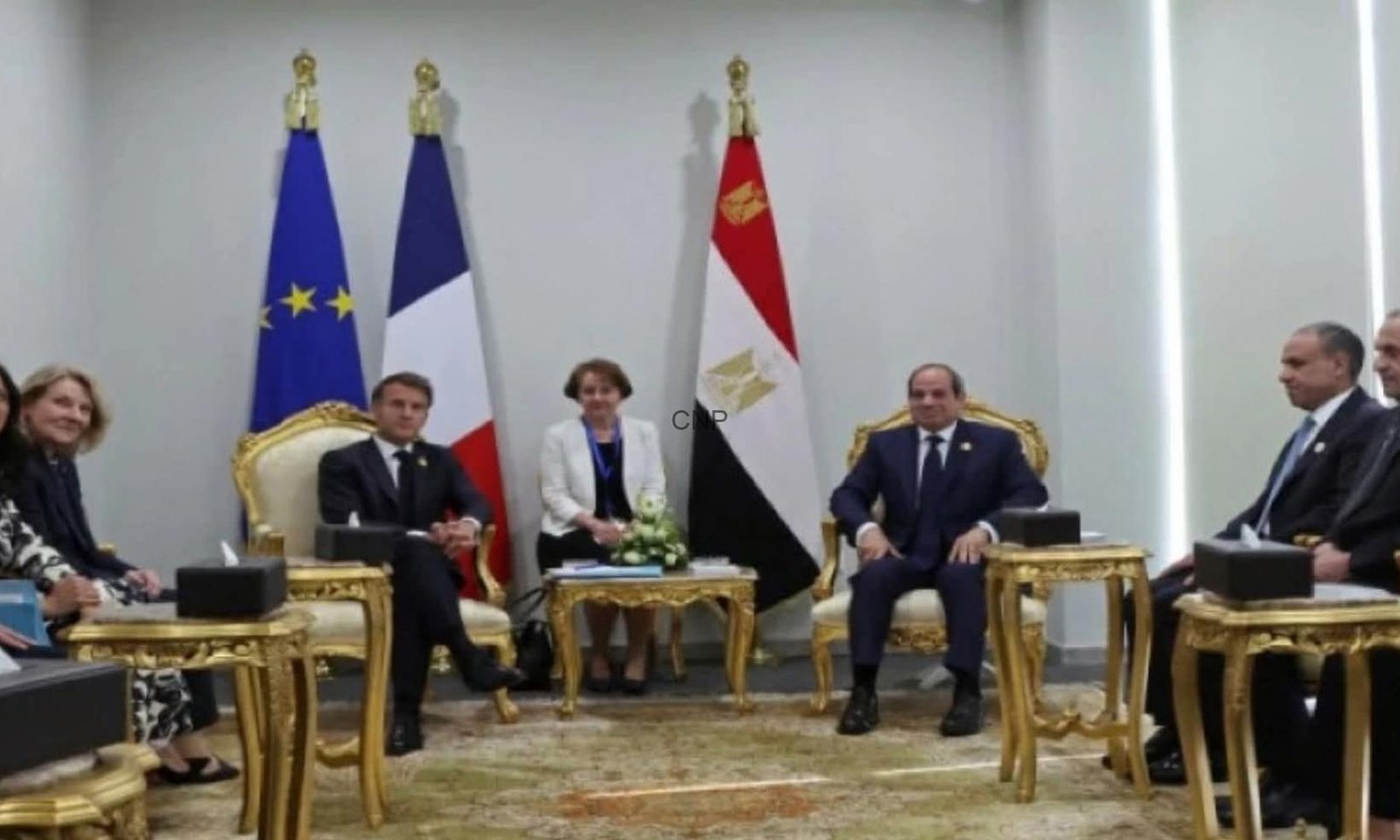 Officials seated in a formal meeting room with European Union, French, and Egyptian flags behind them and ornate gold furniture.