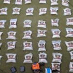Rows of white sacks with a red-and-yellow emblem arranged in neat rows on a green ground, with some equipment (orange device, blue items) near the foreground.