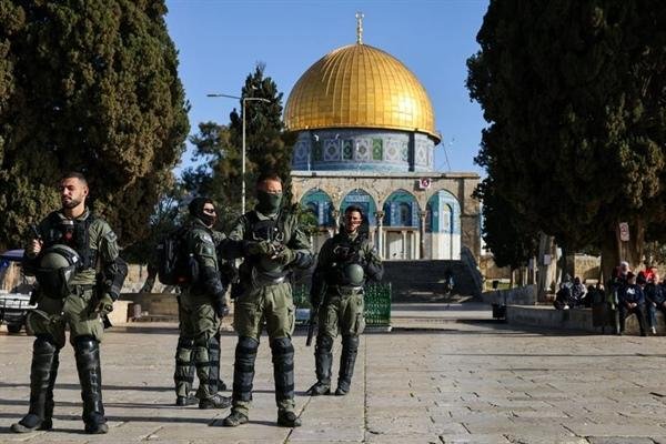 Group of soldiers in tactical gear standing in a stone courtyard with the Golden Dome of the Rock in Jerusalem in the background.