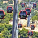 Red gondola cabins of a mountain cable car system crossing a forested hillside.
