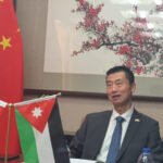Man in a suit sits at a conference table with the Chinese flag and Jordan flag displayed near him during a formal meeting, backdrop shows art and 'CNP' text.