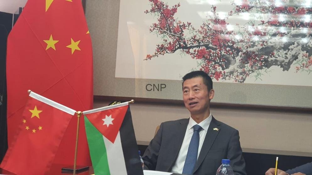 Man in a suit sits at a conference table with the Chinese flag and Jordan flag displayed near him during a formal meeting, backdrop shows art and 'CNP' text.