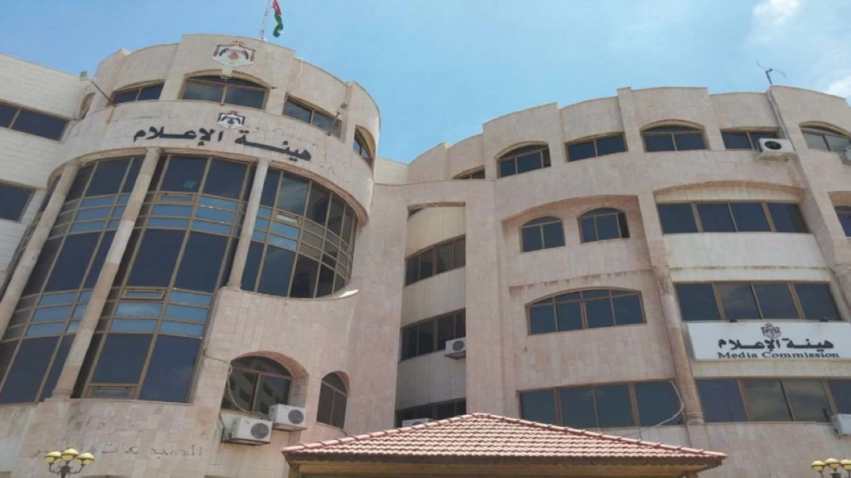 - Center News Network Exterior view of a beige multi-story building with curved glass facade and Arabic sign, under a blue sky (Media Commission building)