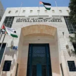Front view of the Central Bank of Jordan building with flagpoles and the Jordanian flag against a blue sky.