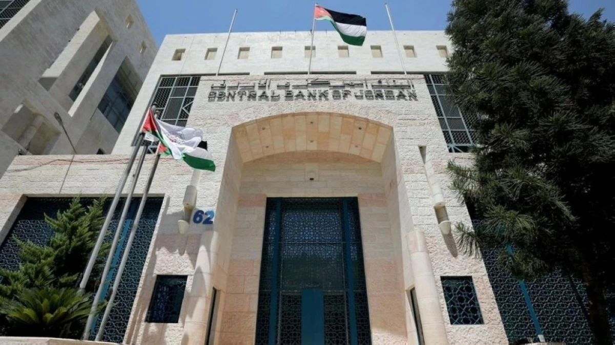 Front view of the Central Bank of Jordan building with flagpoles and the Jordanian flag against a blue sky.