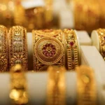 Close-up of ornate gold bangles with red gemstones on a display stand in a jewelry shop.