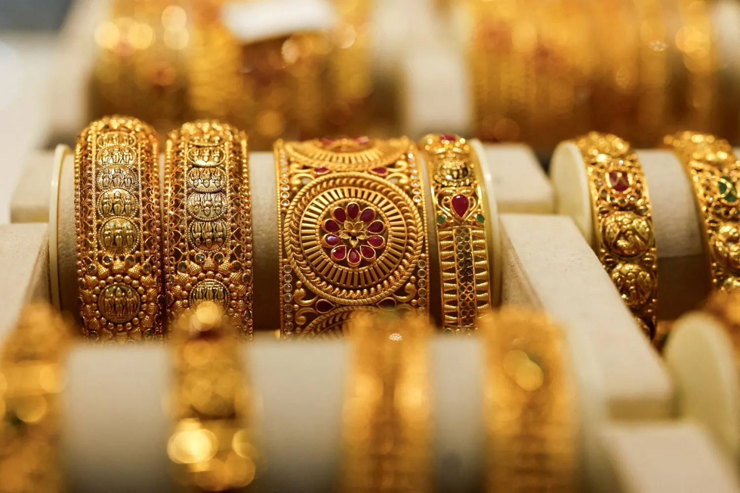 Close-up of ornate gold bangles with red gemstones on a display stand in a jewelry shop.