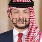 Man wearing a red-and-white checkered ghutra with black agal, navy suit, and red tie in a formal portrait.