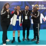 Boxer in blue trunks and red hand wraps posing with three officials in a World Boxing backdrop site.