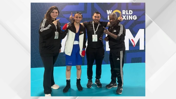 Boxer in blue trunks and red hand wraps posing with three officials in a World Boxing backdrop site.