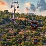 Red gondola cable car gliding over a rocky hillside with sparse vegetation and a blue sky.
