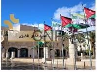 aman - Center News Network Exterior view of a campus building with arched entrance, several flagpoles displaying colorful flags in front, and a yellow logo on the left.