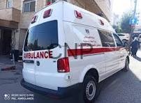 Rear and side view of a white ambulance parked on a city street with red markings and emergency lights visible