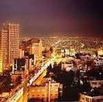 Nighttime city skyline with illuminated buildings and a bright main road cutting through the urban area.