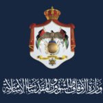 Official government crest on a dark blue background, featuring a crowned shield with an eagle, flags, and Arabic script beneath.