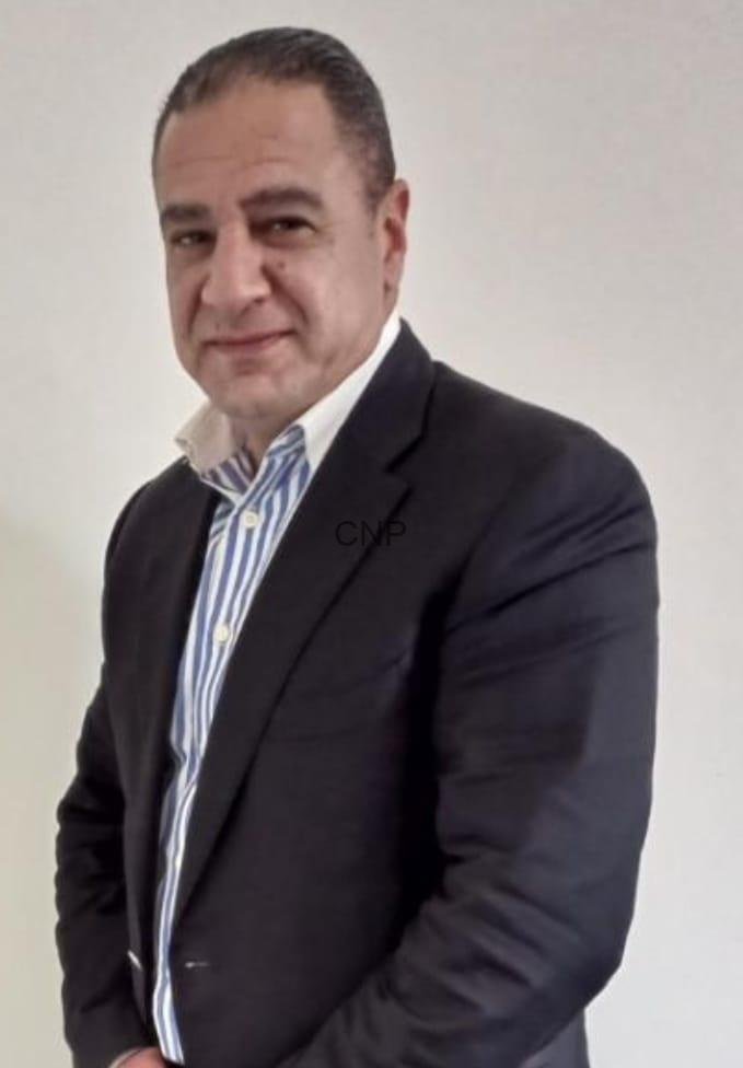 ayman - Center News Network Professional head-and-shoulders portrait of a man in a dark suit and striped shirt against a light background.