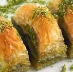 Close-up of three pistachio baklava pieces on a light surface, showing flaky golden pastry and green chopped pistachios.