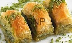 Close-up of three pistachio baklava pieces on a light surface, showing flaky golden pastry and green chopped pistachios.