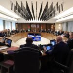 Formal government meeting: officials seated around a large curved table with laptops, central screen, and Jordanian flags in the background.