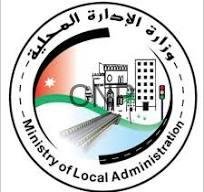 balad - Center News Network Circular seal of the Ministry of Local Administration (Jordan), with Arabic and English text, featuring the Jordanian flag colors, a gate motif, buildings, and a road/rail elements.